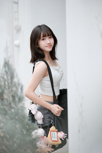 フリー写真 鞄を肩にかけて白い壁の前に立つ台湾人女性