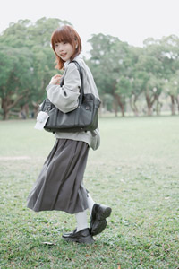 フリー写真 鞄を肩にかけて芝生の上に立つ台湾人女性