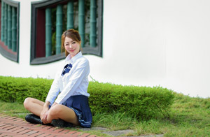 フリー写真 ウインクしながらあぐらをかいて地面に座る女子学生