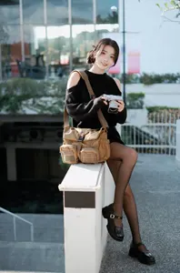 フリー写真 鞄を肩にかけてカメラを持ちながらフェンスに腰掛ける台湾人女性