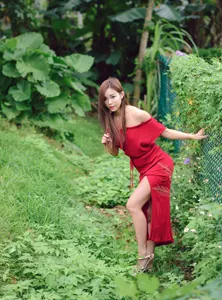 フリー写真 髪の毛を触りながら草が生い茂ったフェンスの前に立つ台湾人女性