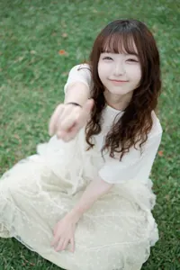フリー写真 芝生の上に座って人差し指を立てる台湾人女性