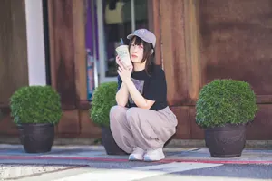フリー写真 紙コップを頬にあててしゃがむ外国人女性
