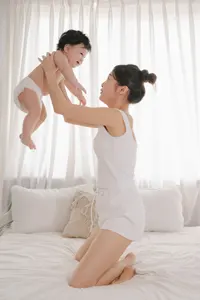 フリー写真 ベッドの上で赤ちゃんを抱き上げるお母さん