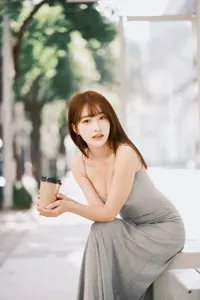 フリー写真 コーヒーが入った紙コップを持ってバスのベンチに座るワンピース姿の台湾人女性