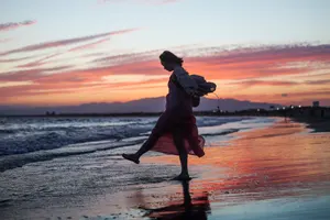 フリー写真 夕暮れの砂浜に立って片足を上げる女性