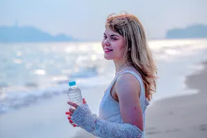 フリー写真 ペットボトルの水を持ってビーチに立つ若い外国人女性